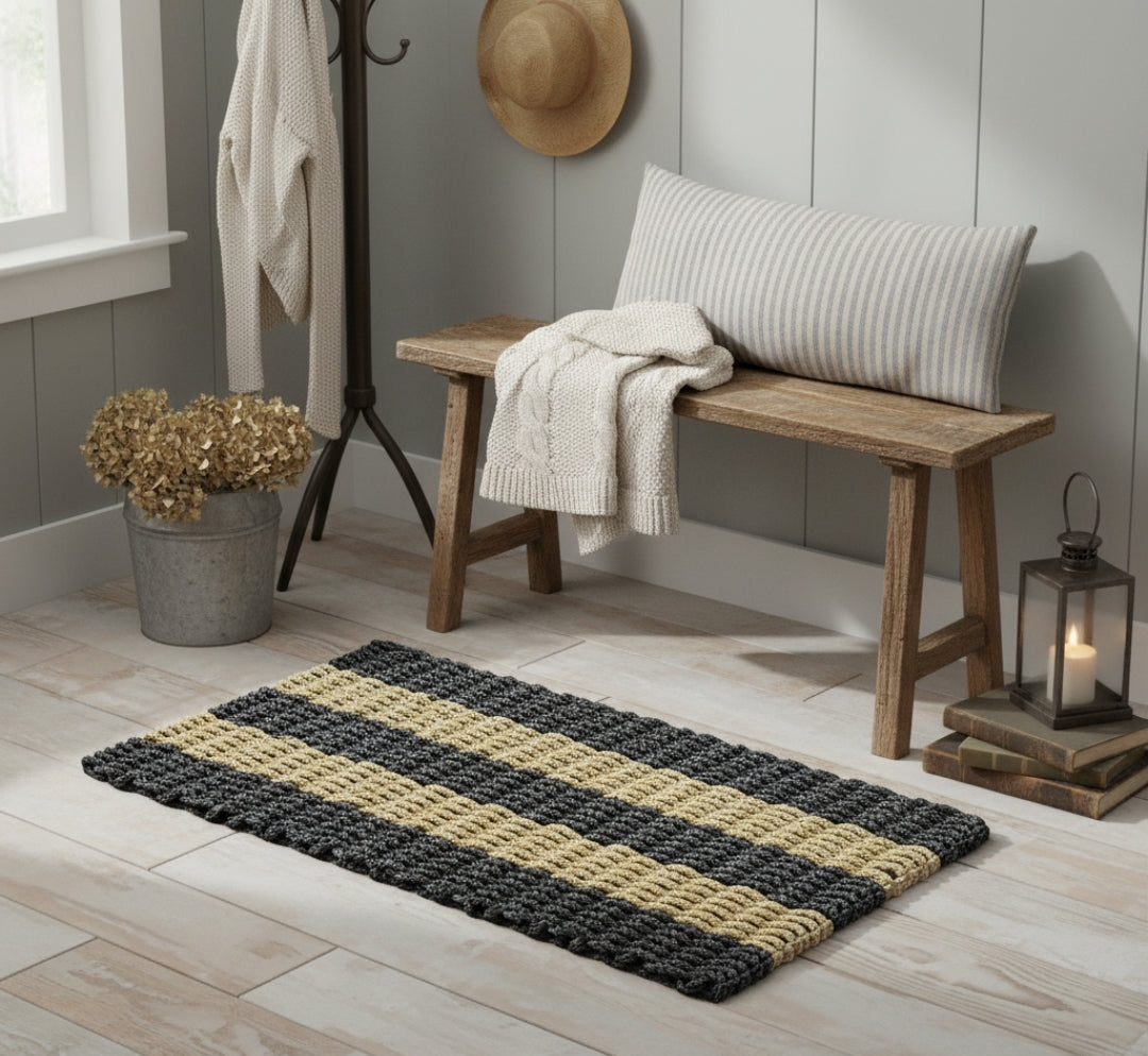 Rustic-themed rug with black and beige stripes on a wooden floor, with a bench and decorative items in the background.