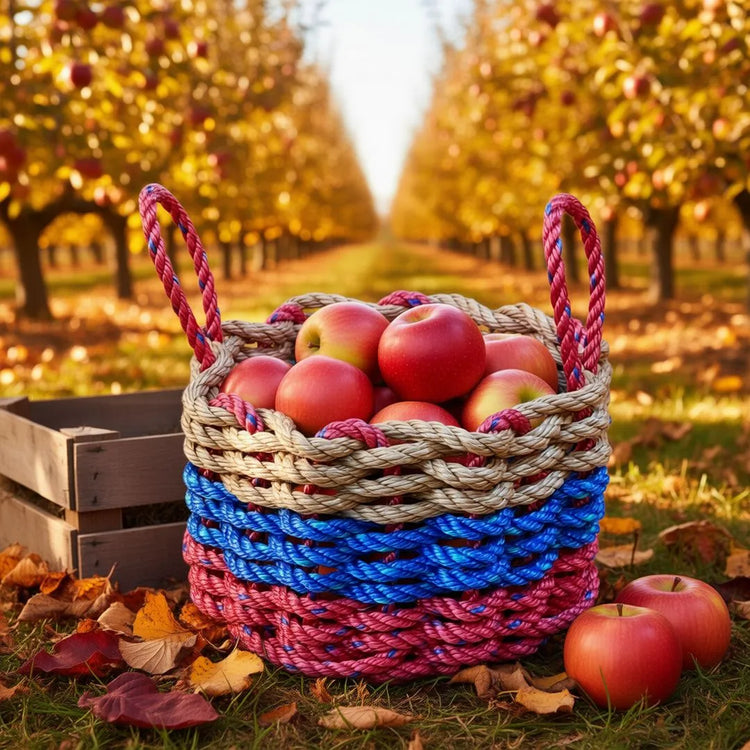 Handwoven red, blue, and tan rope basket filled with red apples in an orchard