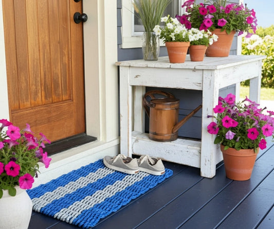 Front porch with a wooden door, white bench, blue and white doormat, and potted flowers.