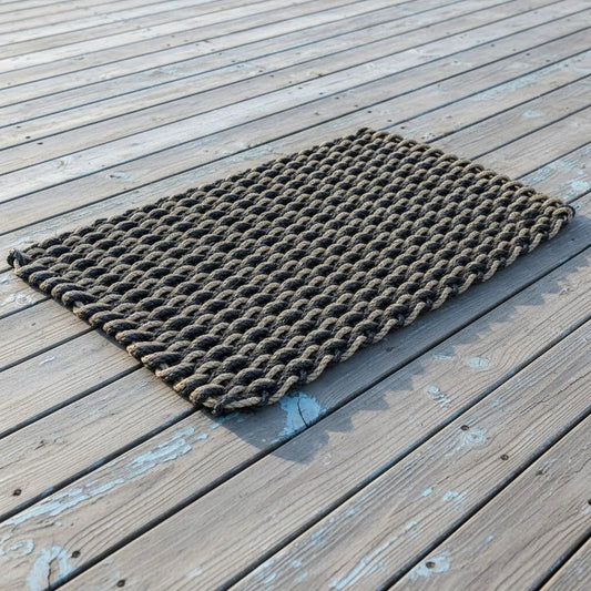 Black and tan double weave lobster rope doormat on weathered wooden decking, showing its interwoven pattern.