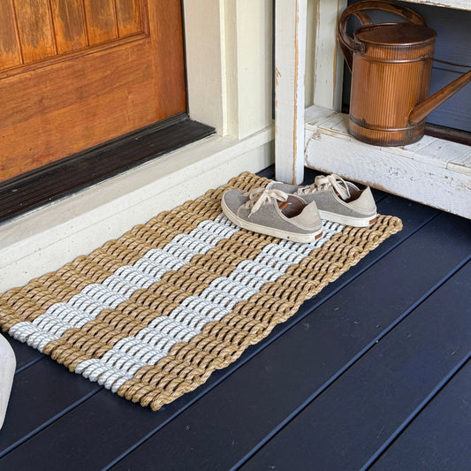 Doormat with five striped pattern on a porch deck shoes on top, and a wooden door in the background.