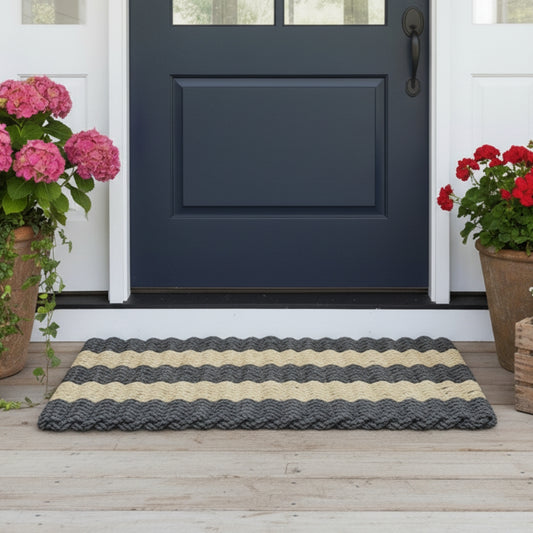 Handcrafted black and tan farmhouse style doormat on a wooden floor, flanked by potted plants.