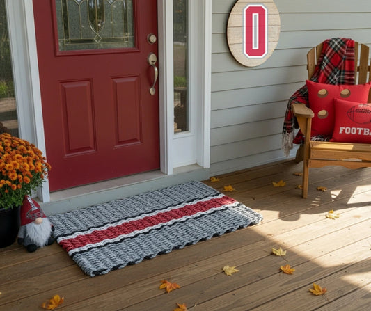 Front porch with a red door, doormat, and decorative items on a wooden deck.