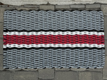 Doormat with a woven pattern featuring gray, red, and black colors on a stone floor.