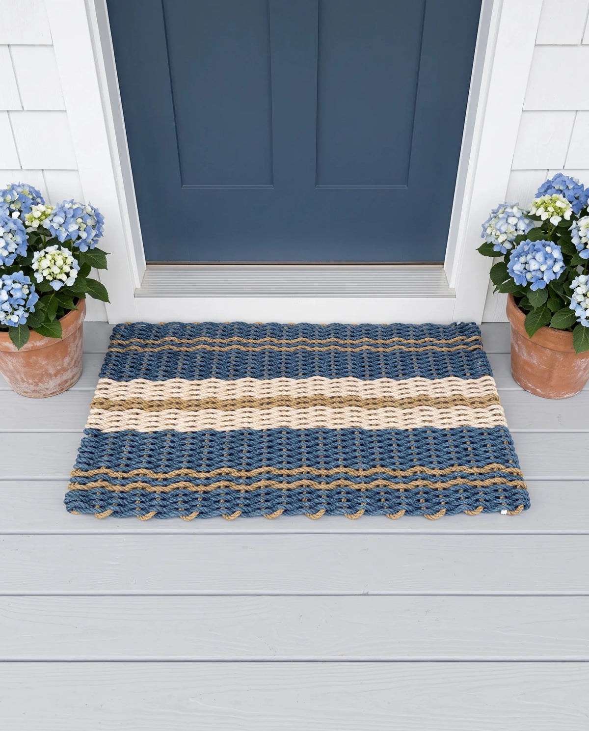 The Admiral lobster rope doormat showing its blue, tan and sand palette in an outdoor setting.