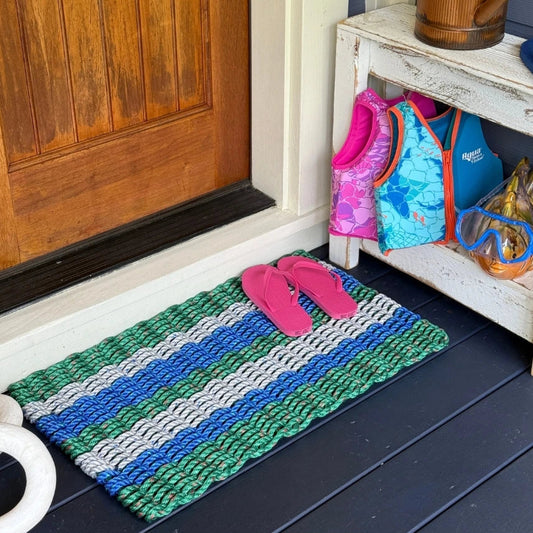 Colorful lobster rope doormat with beachy shoes on a wooden porch next to a wooden door.
