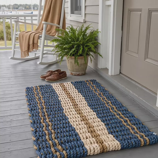 The Admiral Lobster Rope Doormat in blue, tan and sand, with paired tan stripes and a broad sand center band.
